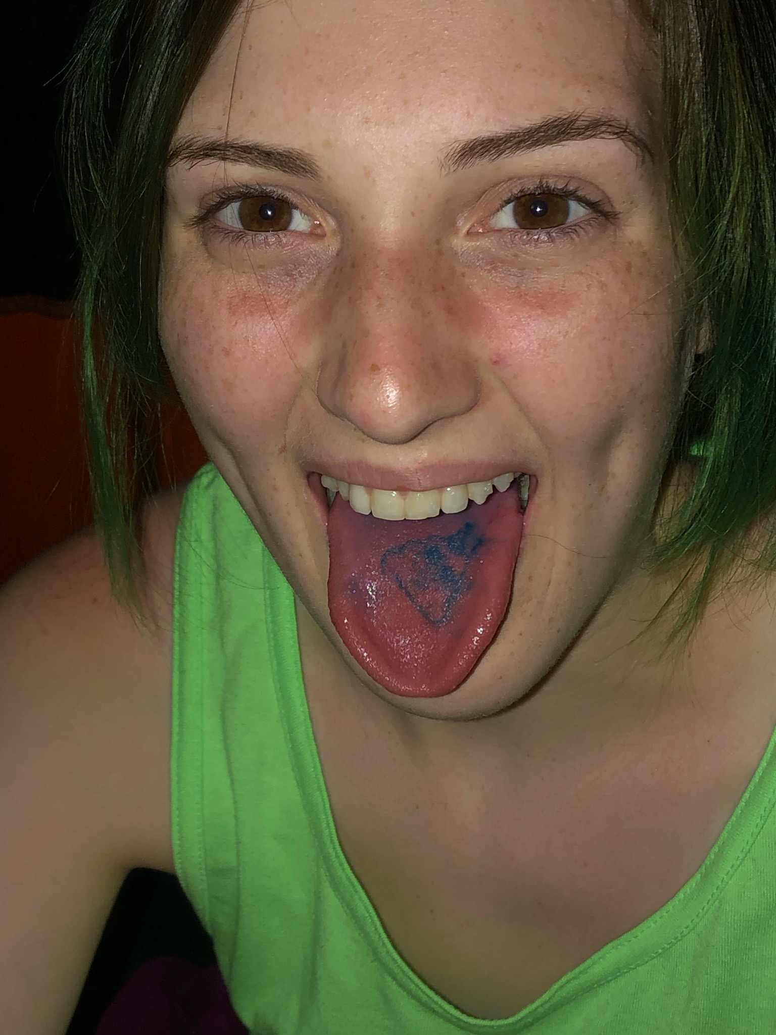 Ashley with her tongue out. On her tongue is a blue poop emoji.